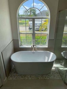 Elegant freestanding bathtub in bright modern bathroom with large arched window, offering a relaxing escape and enhancing home interior style. Luxury freestanding bathtub with view of lush backyard, ideal for relaxing baths, high-end bathroom renovation, and modern house design. Perfect for home spa and wellness upgrades.