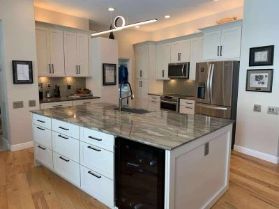 Elegant kitchen with white cabinets, granite island, stainless steel fridge, and built-in microwave, perfect for modern living and home improvement projects by Days Home Solutions. High-quality modern kitchen featuring a spacious island with a granite countertop, stainless steel appliances, white cabinetry, and hardwood floors, showcasing home renovation with Days Home Solutions.