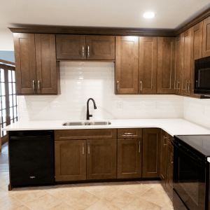 Beautiful kitchen with dark wood cabinetry, white countertops, and stainless steel sink, perfect for home renovation or kitchen upgrades. Stainless steel kitchen sink with black faucet and dark wood cabinets in a modern kitchen.