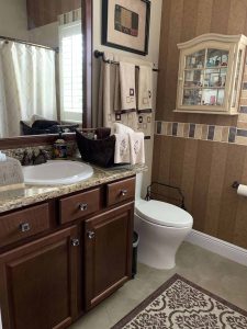 Bathroom with wood cabinets and granite countertop featuring decorative towels, wall cabinet, and a comfortable, stylish design. Modern bathroom with wooden cabinetry, granite countertop, white toilet, framed mirror, decorative towels, wall cabinet, patterned tile, and a small window for natural light.