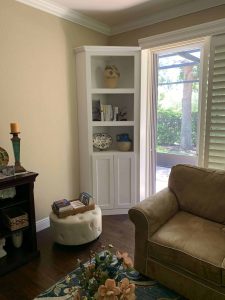 White corner bookshelf with storage cabinets, decorative pottery, and books in a bright living space. Vintage white corner bookshelf with decorative items and books in a cozy living room setting.