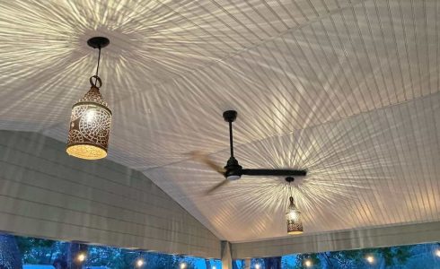 Stylish outdoor ceiling with decorative lighting and a ceiling fan, perfect for enhancing your home's outdoor entertainment area. Decorative pendant lights casting intricate shadows on the ceiling of a screened porch, creating a warm and inviting outdoor living space.